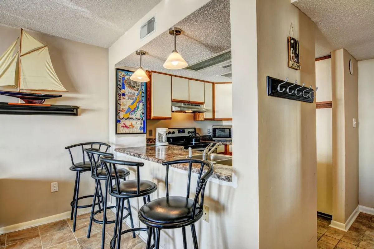 A casual and relaxed kitchen and dining setup featuring bar stools at a countertop, nautical sailboat decor, and colorful wall art. The space suggests a warm atmosphere ideal for sharing casual meals and celebrating special occasions.