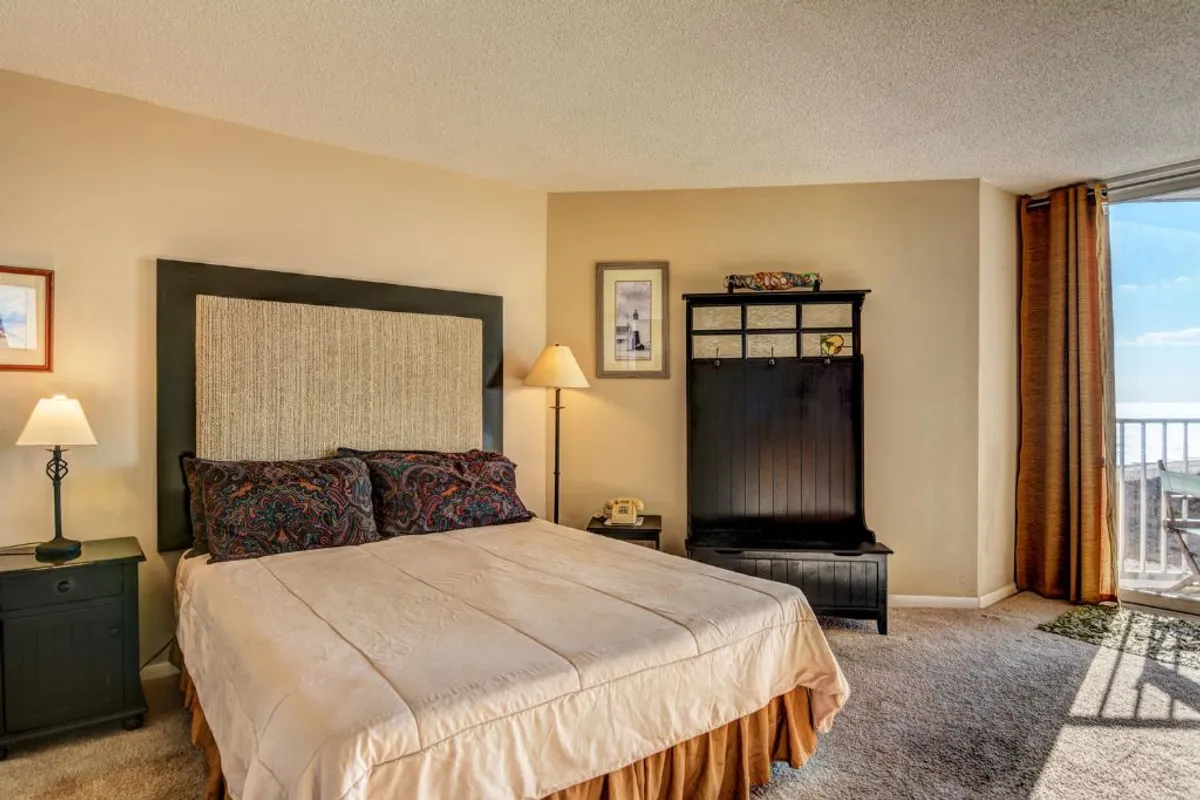 This image presents a cozy bedroom featuring a comfortable bed, a nightstand with a lamp for evening reading, and a black wooden coat rack. The overall decor is calm and inviting, with soft lighting that enhances the tranquil atmosphere, perfect for unwinding after a busy day.