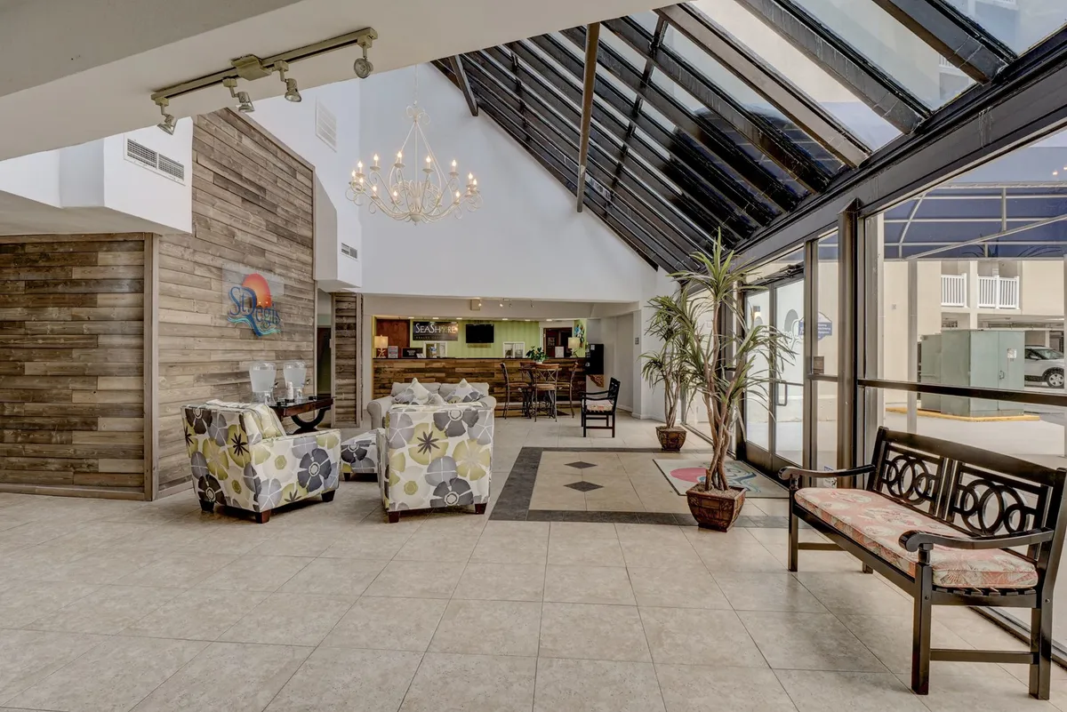 A welcoming reception area featuring a chandelier, reception desk, comfortable seating, and expansive windows that fill the space with natural light. The ambiance is inviting, hinting at the resort's full-service amenities and a sense of arrival for guests.
