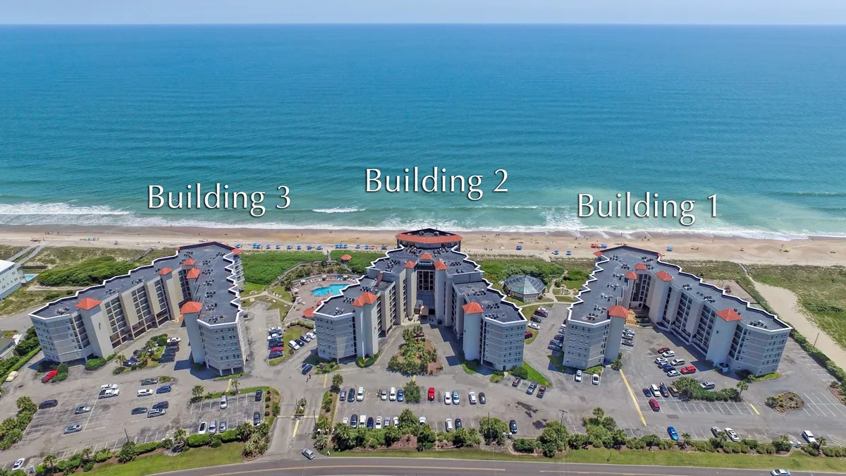 A sweeping exterior view showcases three resort buildings overlooking an inviting swimming pool, with the vast Atlantic Ocean glimmering in the background. The pool area features plenty of space for lounging and socializing, while the scene is bathed in soft, natural light, suggesting the tranquility of a coastal retreat.