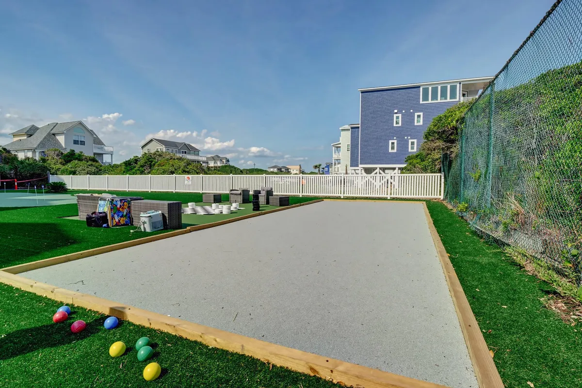 A bocce ball court with colorful balls is surrounded by neighboring homes and a fenced yard, setting the stage for casual yet spirited games. The image evokes a sense of playful competition and leisurely time spent outdoors with family or friends.
