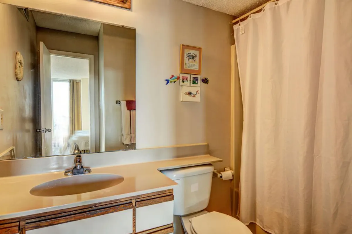 A bright, well-kept bathroom with a mirror, sink, toilet, and shower curtain, complemented by tasteful wall decor. The space feels fresh and inviting, ideal for personal relaxation and daily routines.
